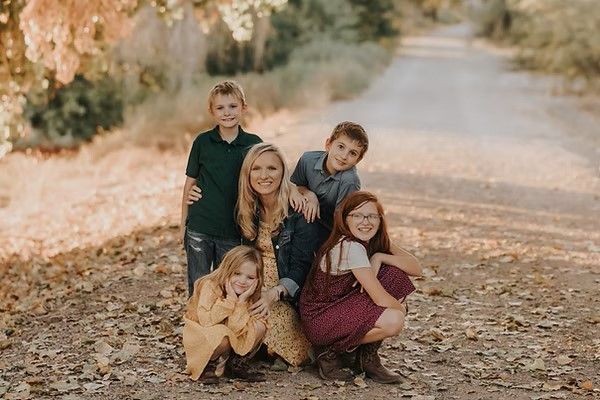 Family poses on path in forest: woman with four children, smiling. Fall colors, leaves on ground.
