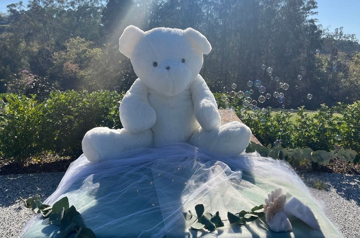 Image of a large teddy bear sitting on material in a garden
