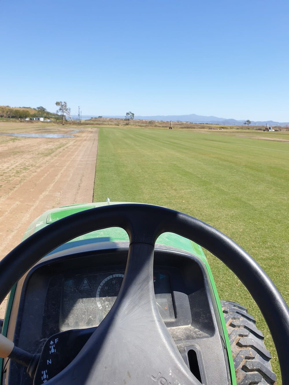 A Green Tractor Is Driving Down A Dirt Road — Marian Lawns In Cannonvale, QLD