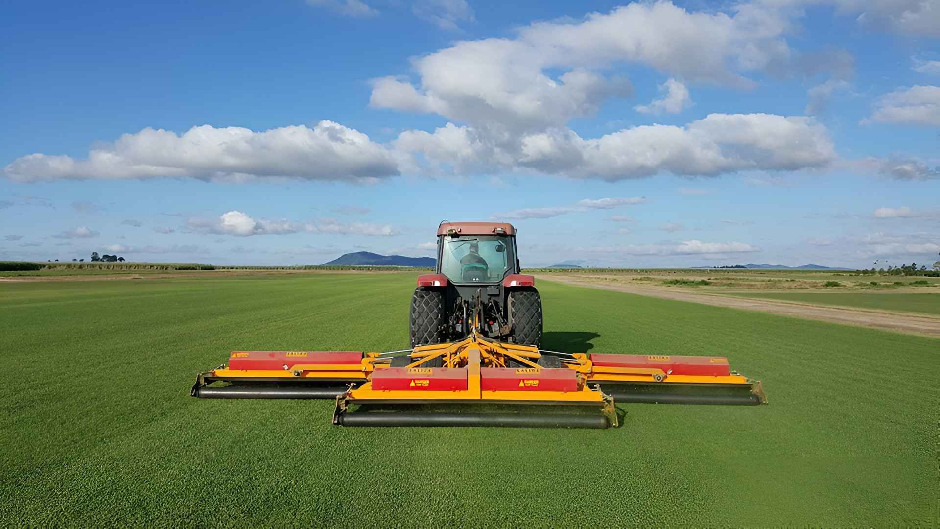 A Tractor Is Cutting Grass In A Field On A Sunny Day — Marian Lawns In Marian, QLD