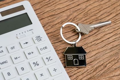 A house keychain is sitting next to a calculator on a wooden table.