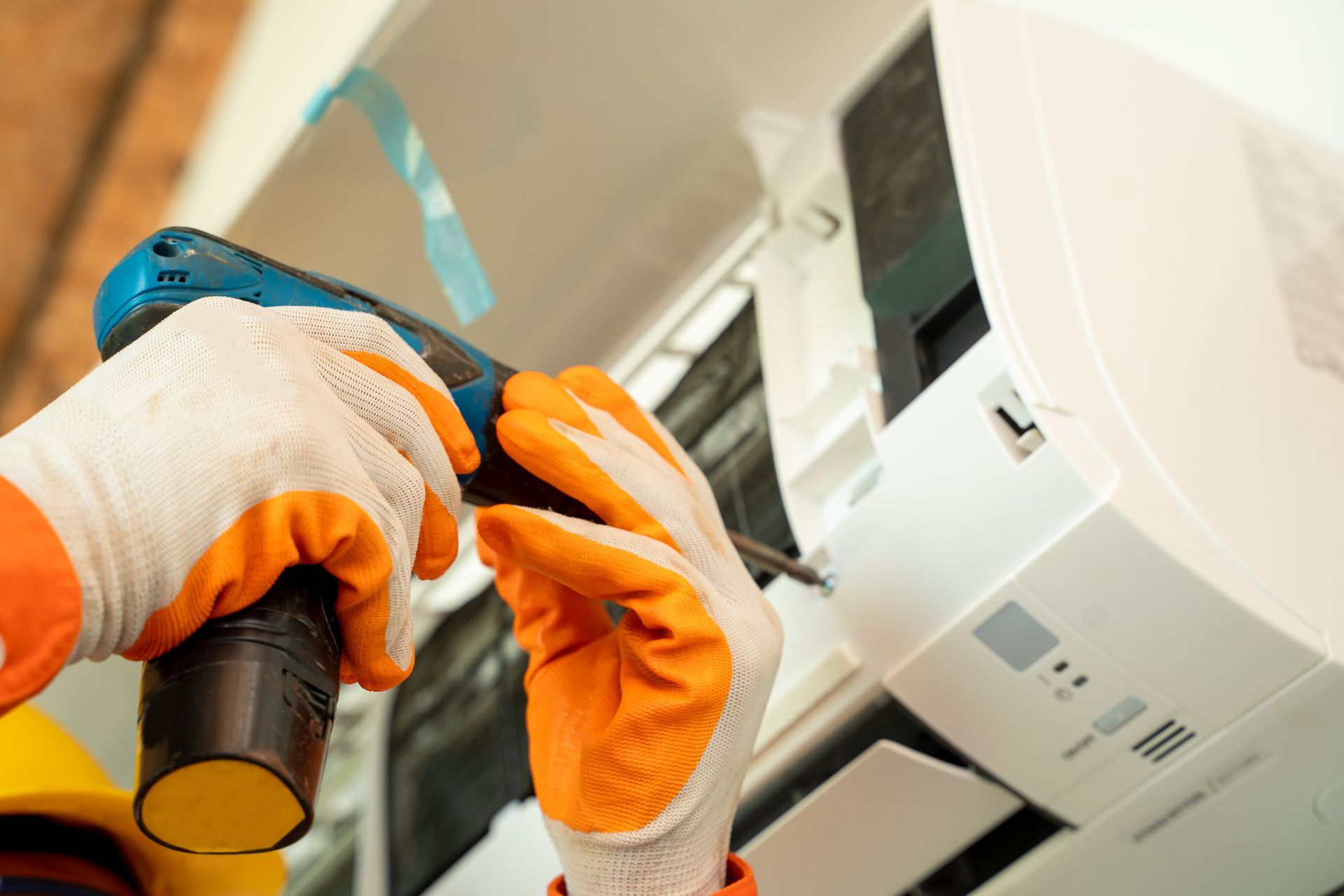 Person wearing gloves using a power drill to repair an air conditioner.