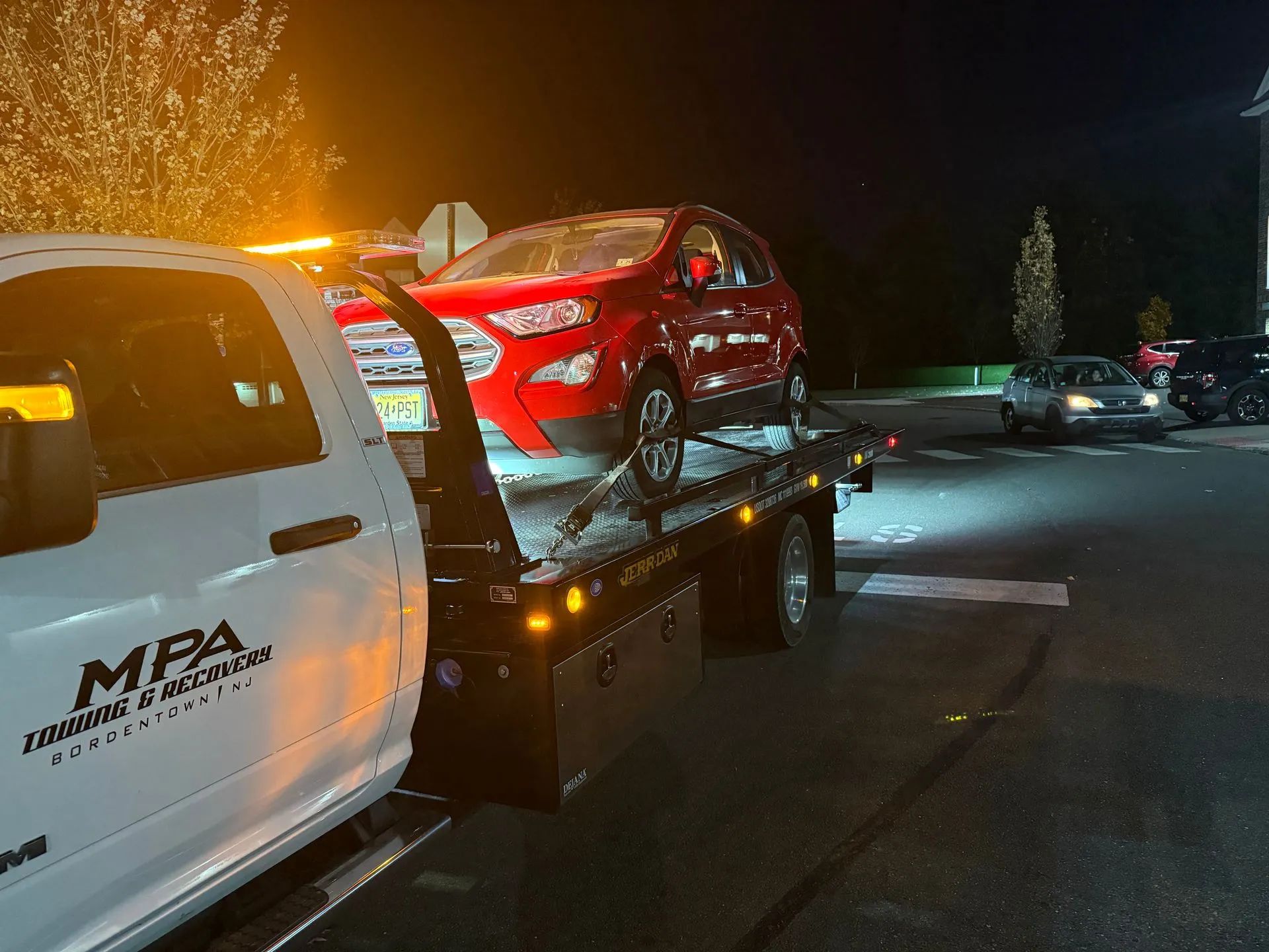 Red SUV on a tow truck at night, parked on a street. Tow truck has flashing lights.