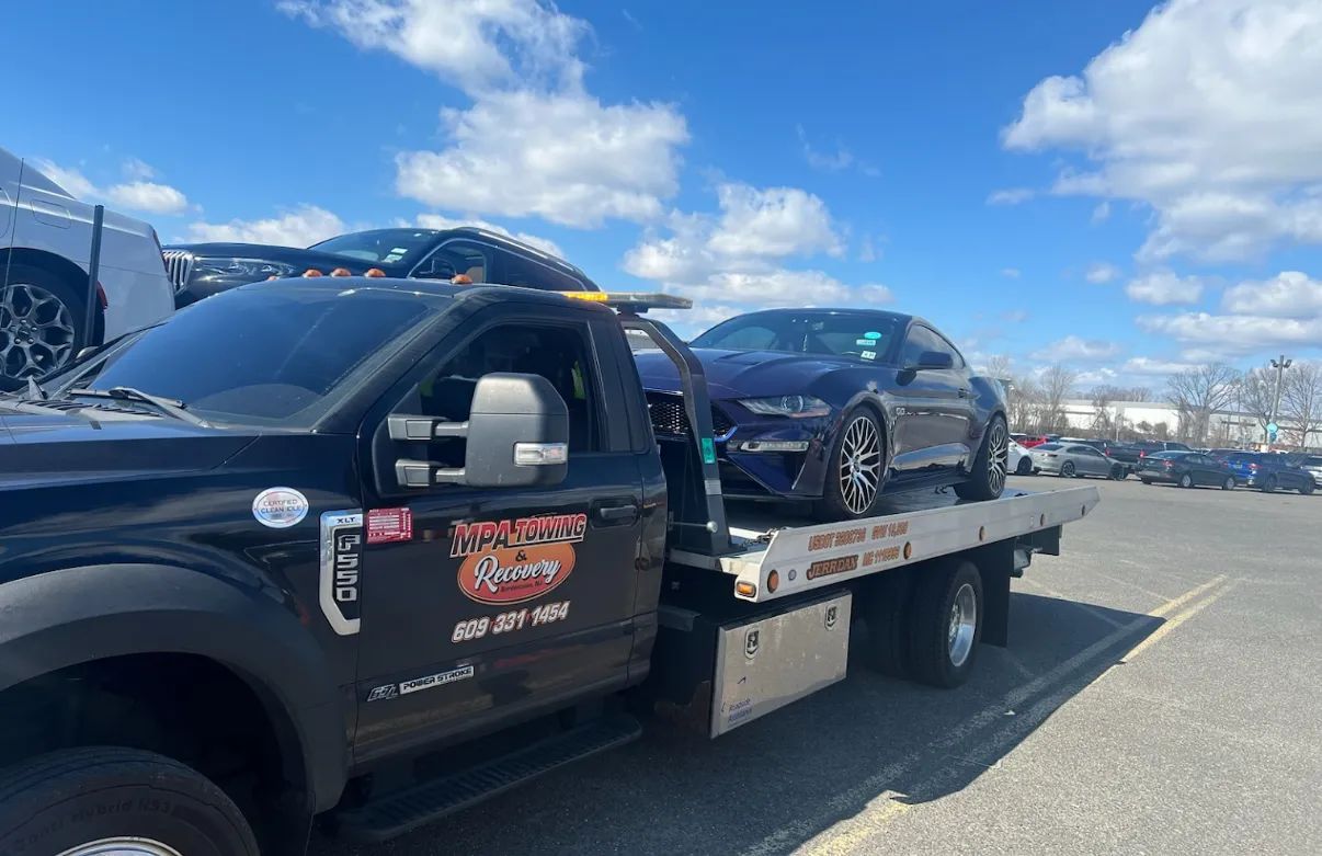 Tow truck carrying a dark blue car on a sunny day.