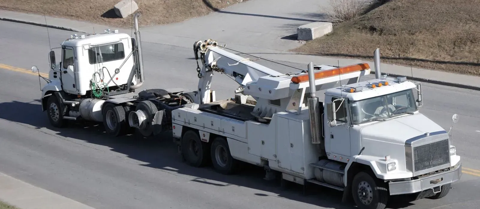 A white tow truck is driving down the road next to a white truck.