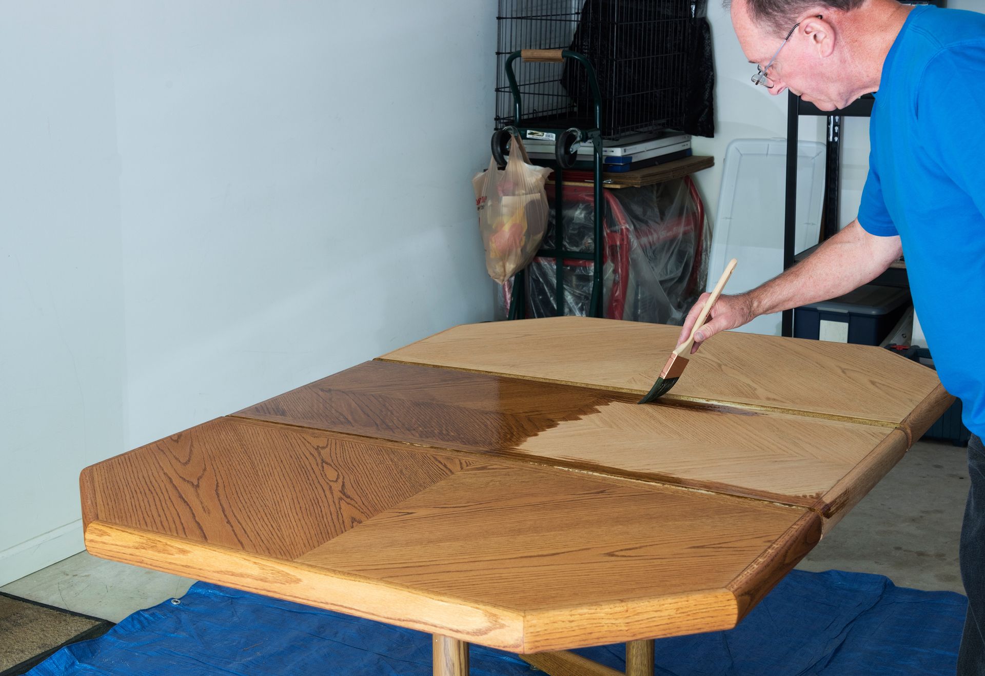 Man meticulously staining a wooden tabletop with a brush, enhancing its rich and deep color.