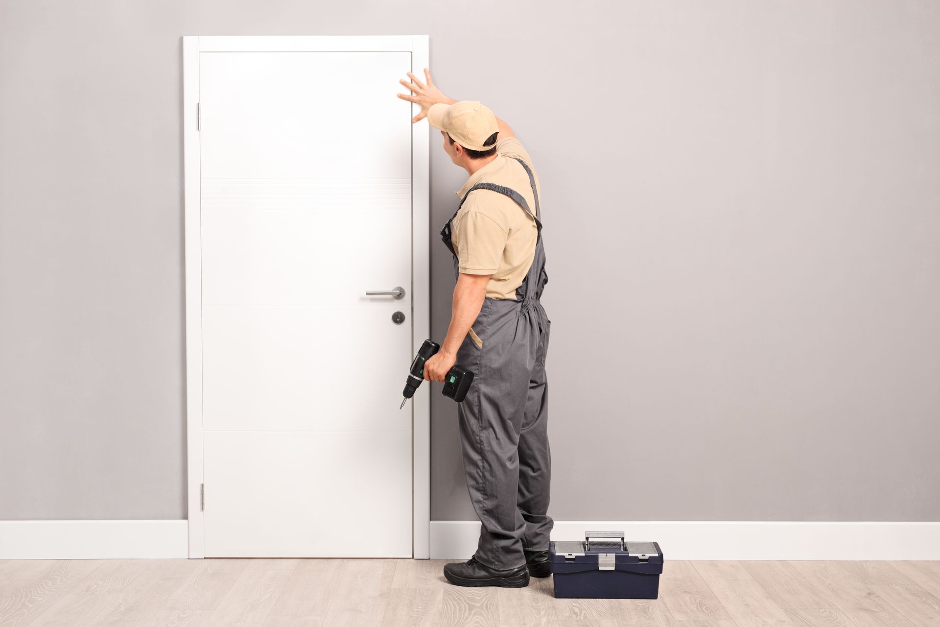 A young handyman in uniform is installing a wooden door.