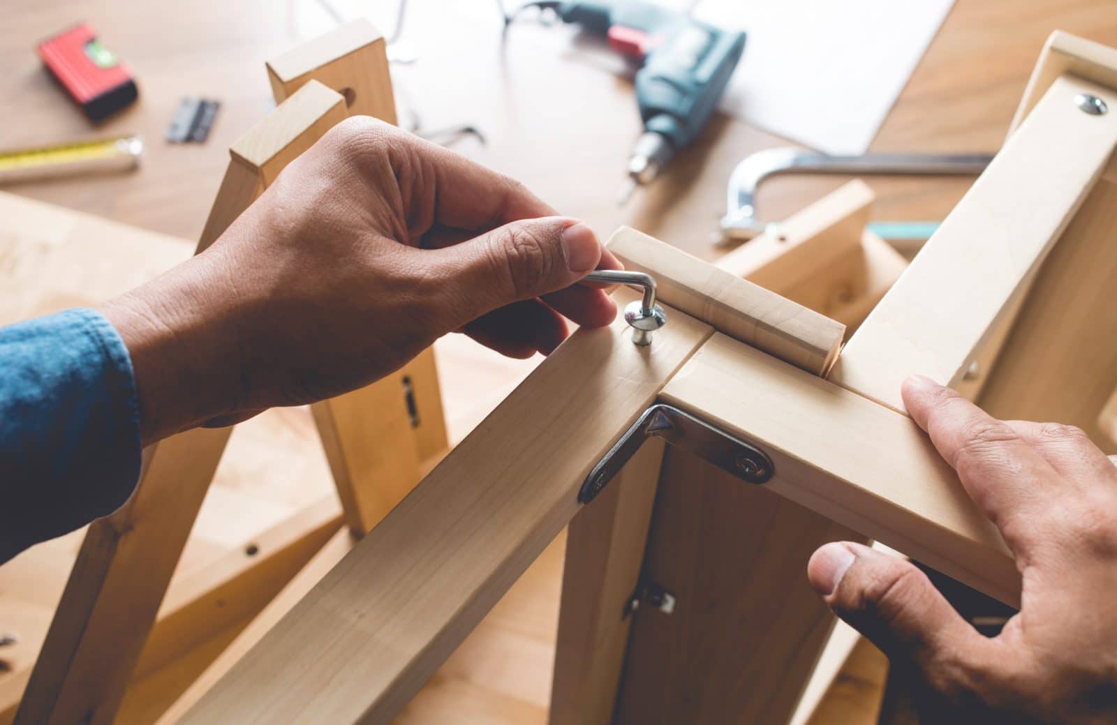 Person assembling furniture using a screwdriver and following instructions.