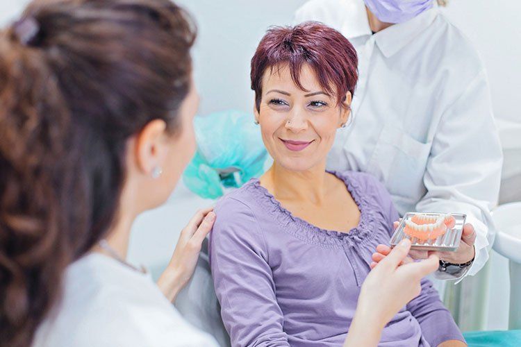 Dentist showing dental model to a patient in a clinic. Both are smiling.
