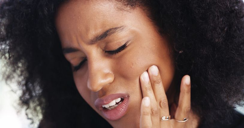 Woman with closed eyes, touching cheek, showing discomfort from possible toothache.