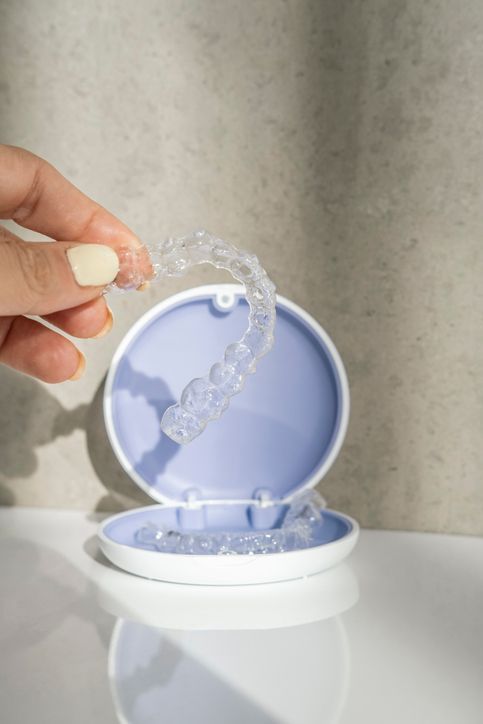 Hand holding clear dental aligner above open case on white surface.