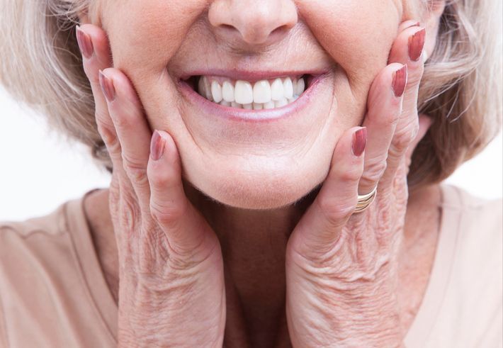 Close-up of a smiling person's face, holding their cheeks with both hands, showing bright white teeth.