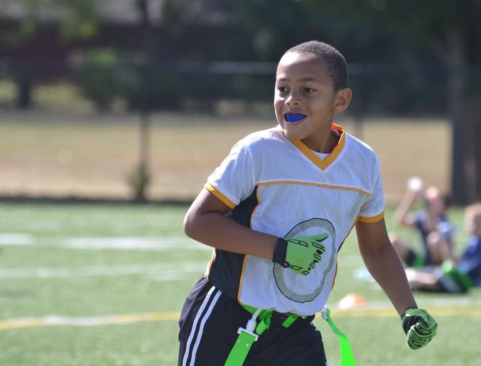 Boy in flag football uniform running on a field, mouth guard in, catching his breath.