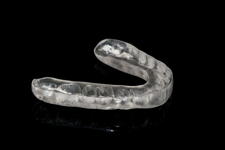Clear, transparent dental mouth guard on a black surface.