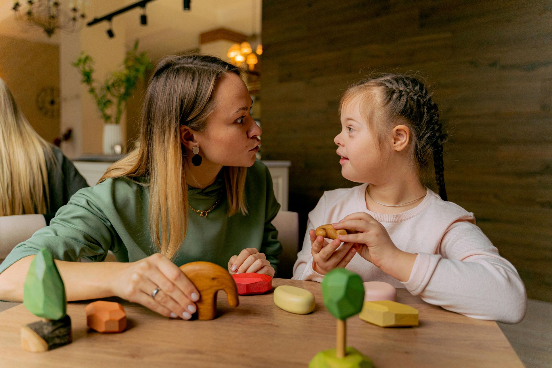 Woman and child with Down syndrome playing with wooden toys at a table indoors.