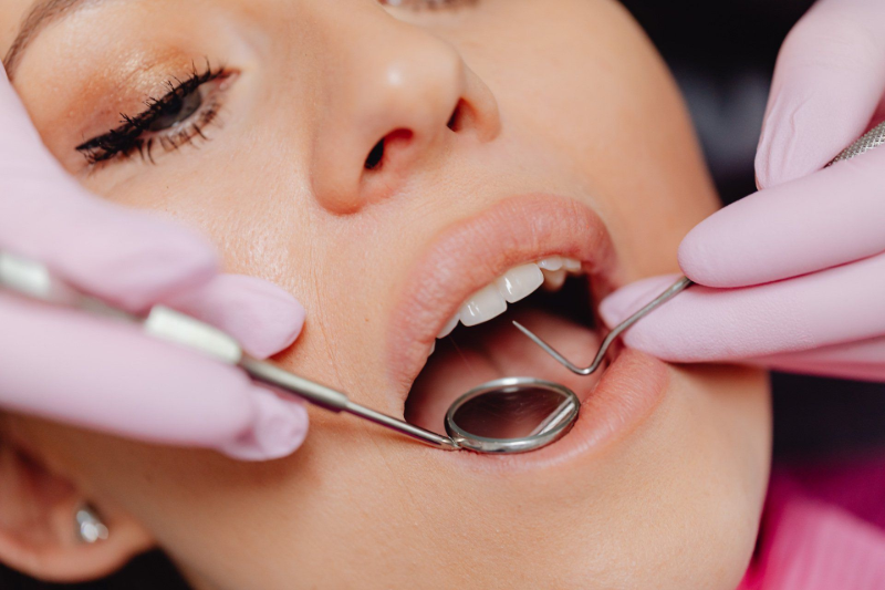 Woman at dental appointment, mouth open, tools in use; pink gloves.