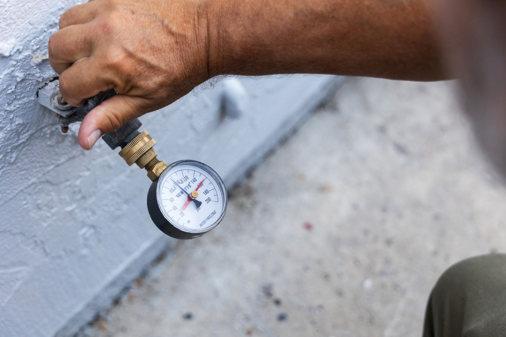 Hand holding a gauge to check water pressure on an outdoor faucet connection.