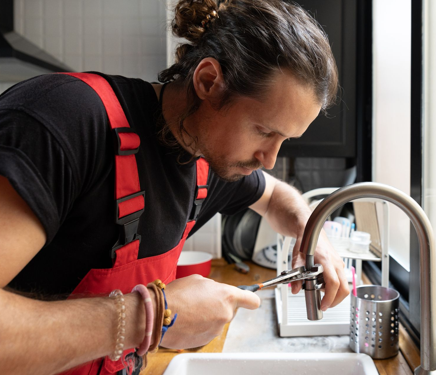 A plumber in red overalls fixes the kitchen faucet.
