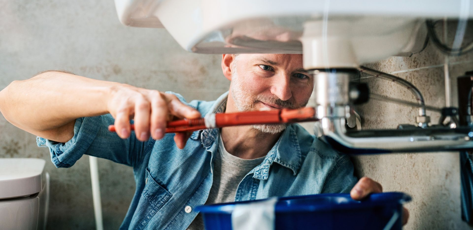 Man trying to fix a leak in a sink using a pipe wrench