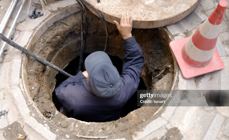 A man in a hole repairing a drain as part of essential emergency sewer cleaning work.