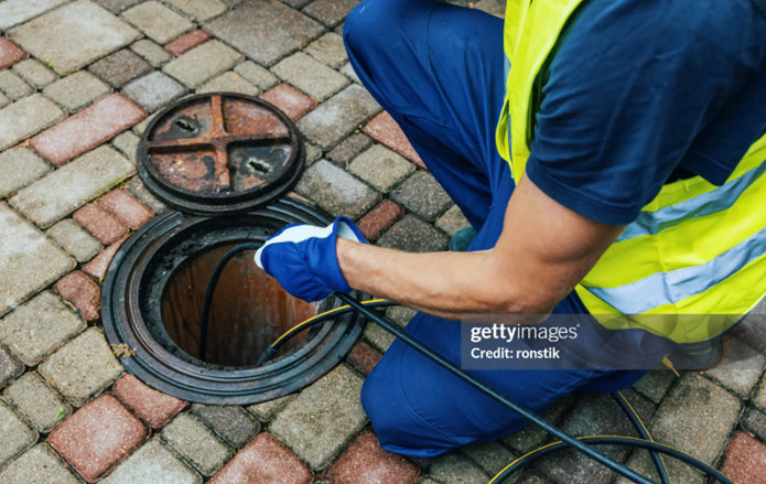 A man in a safety vest repairing a drain as part of essential emergency sewer cleaning work.