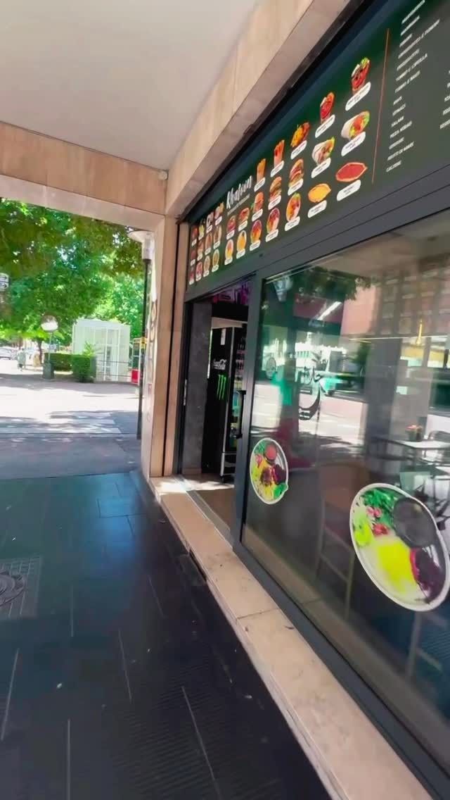 Esterno di un ristorante con menù e vetrina con immagini di piatti. Alberi visibili sullo sfondo.