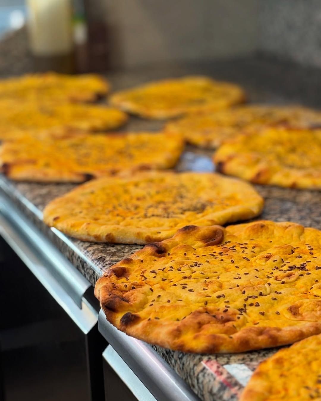 Focacce disposte su un piano di lavoro, con crosta dorata e semi neri sparsi.