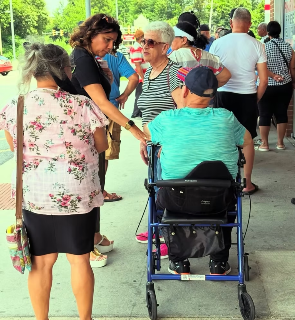 A group of people standing outside, including an individual using a blue wheeled walker.