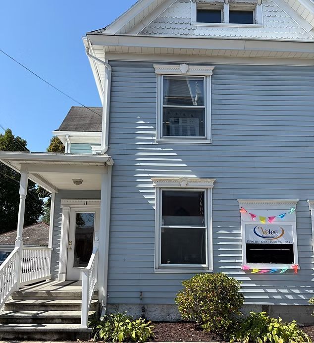 A light blue two-story house with a white front porch, stairs, and a sign in the window with colorful bunting.