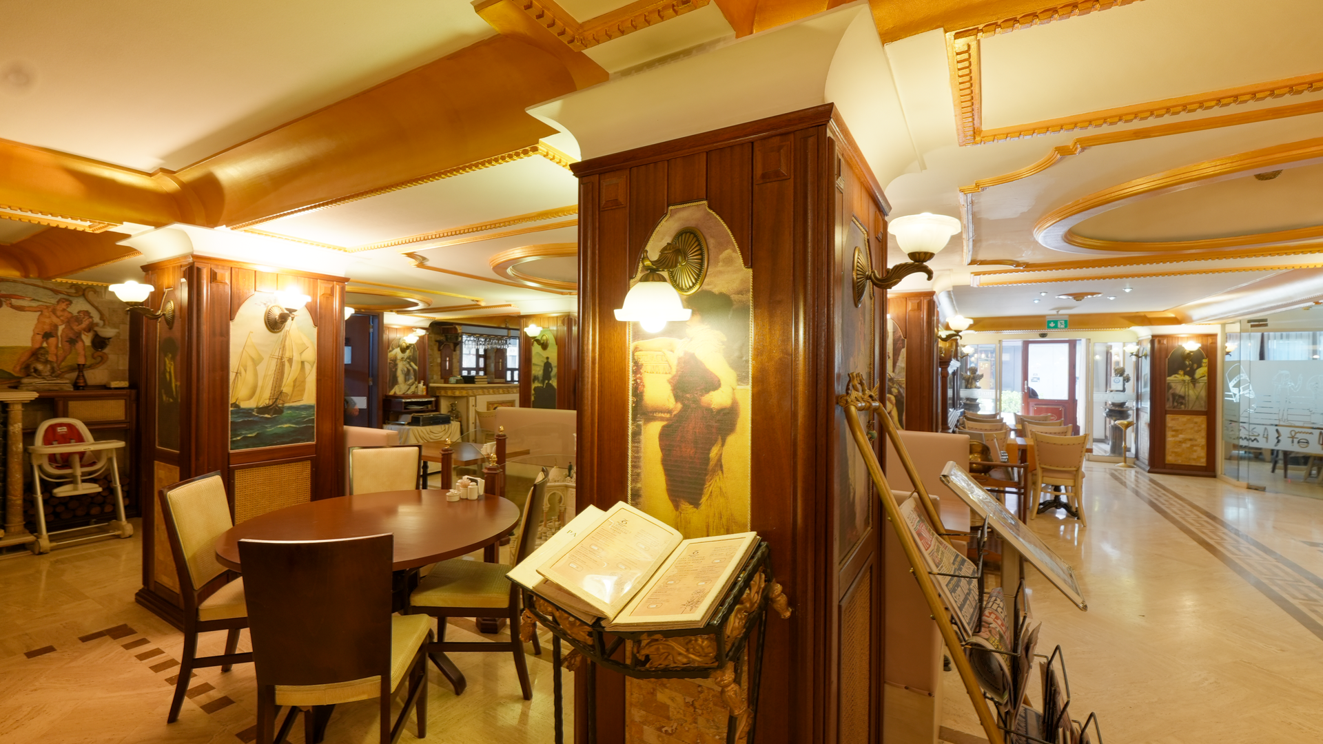 A warmly lit, elegant restaurant interior with ornate wooden columns, a central table, and an open menu stand.