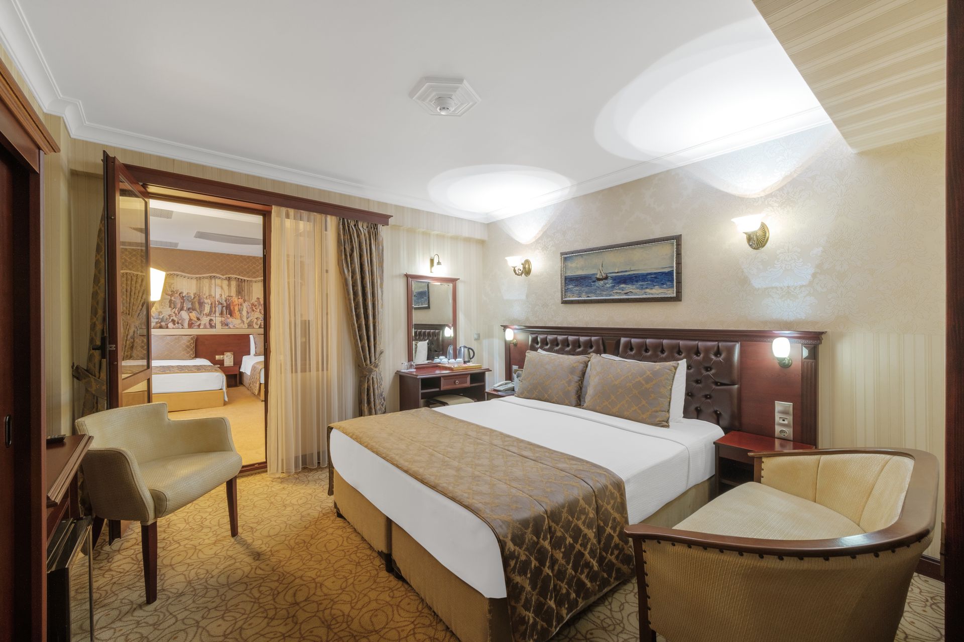 İzmir Park Hotel's featuring a large bed with a brown runner, two armchairs, a wall-mounted landscape painting, and curtains.