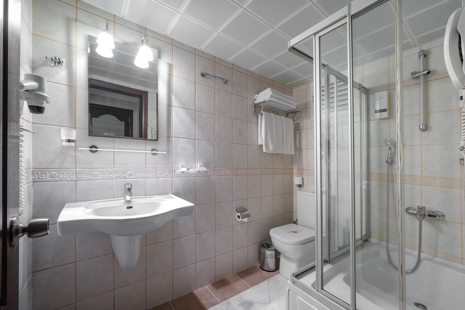A clean, modern bathroom with white wall tiles, a pedestal sink, a toilet, and a glass-enclosed shower stall.