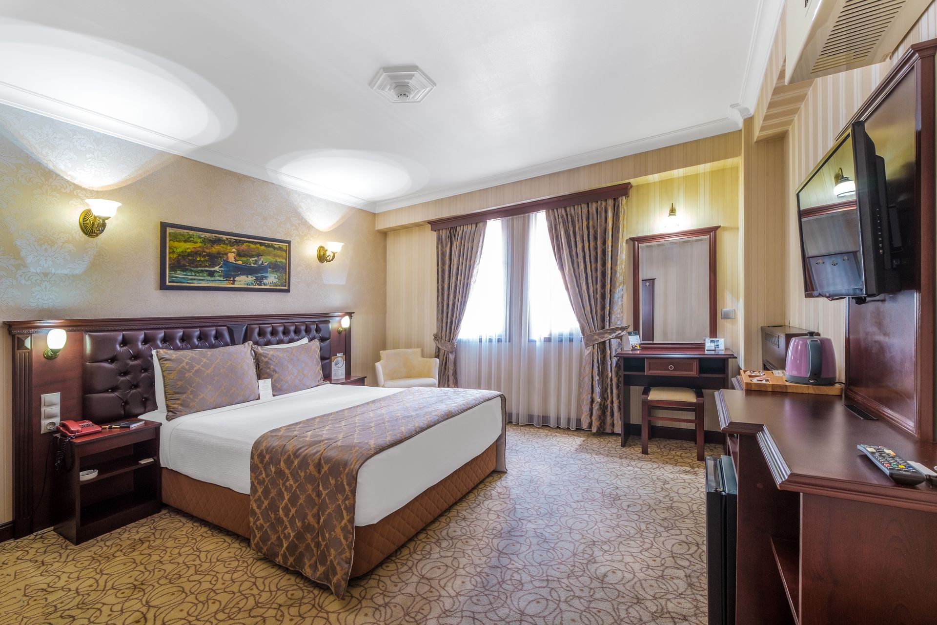 İzmir Park Hotel's room with a queen bed, dark wood furniture, a desk with a vanity mirror, and light patterned carpeting.