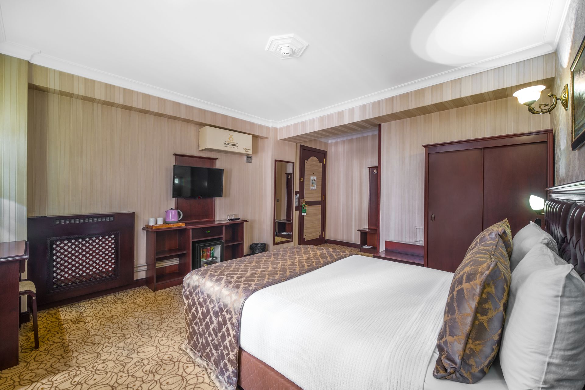 İzmir Park Hotel's room with a queen bed, dark wood wardrobe, television, and patterned carpeting.