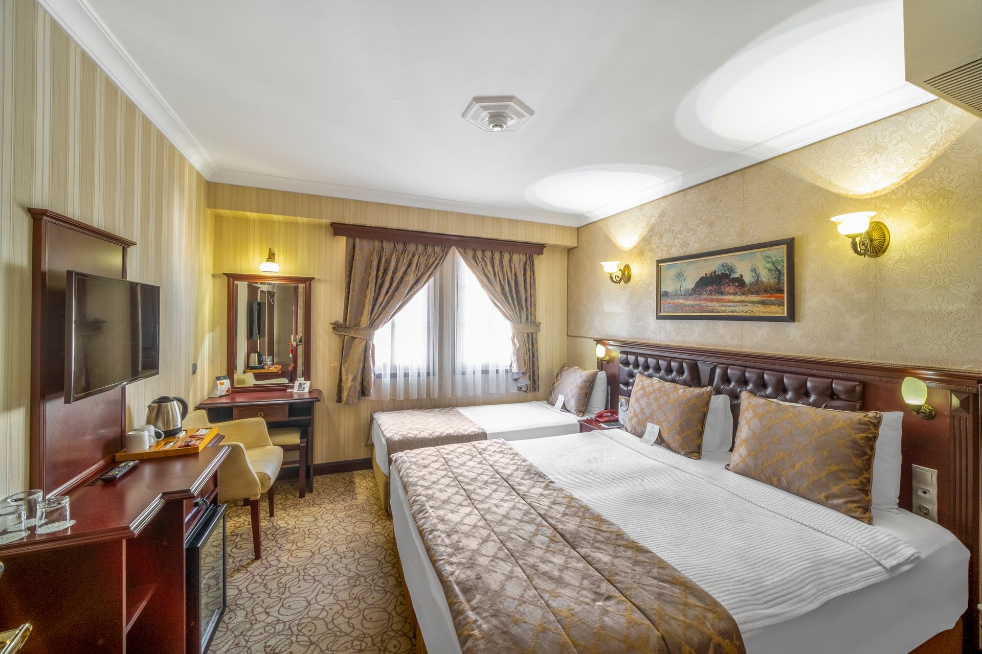 İzmir Park Hotel's room featuring a double bed and a single bed with beige bedding, wooden furniture, and warm wall lighting.