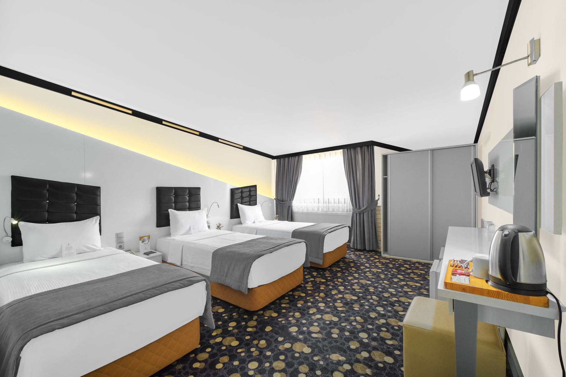 İzmir Park Hotel's modern room with two twin beds, patterned carpeting, grey curtains, and a small desk area with a kettle.