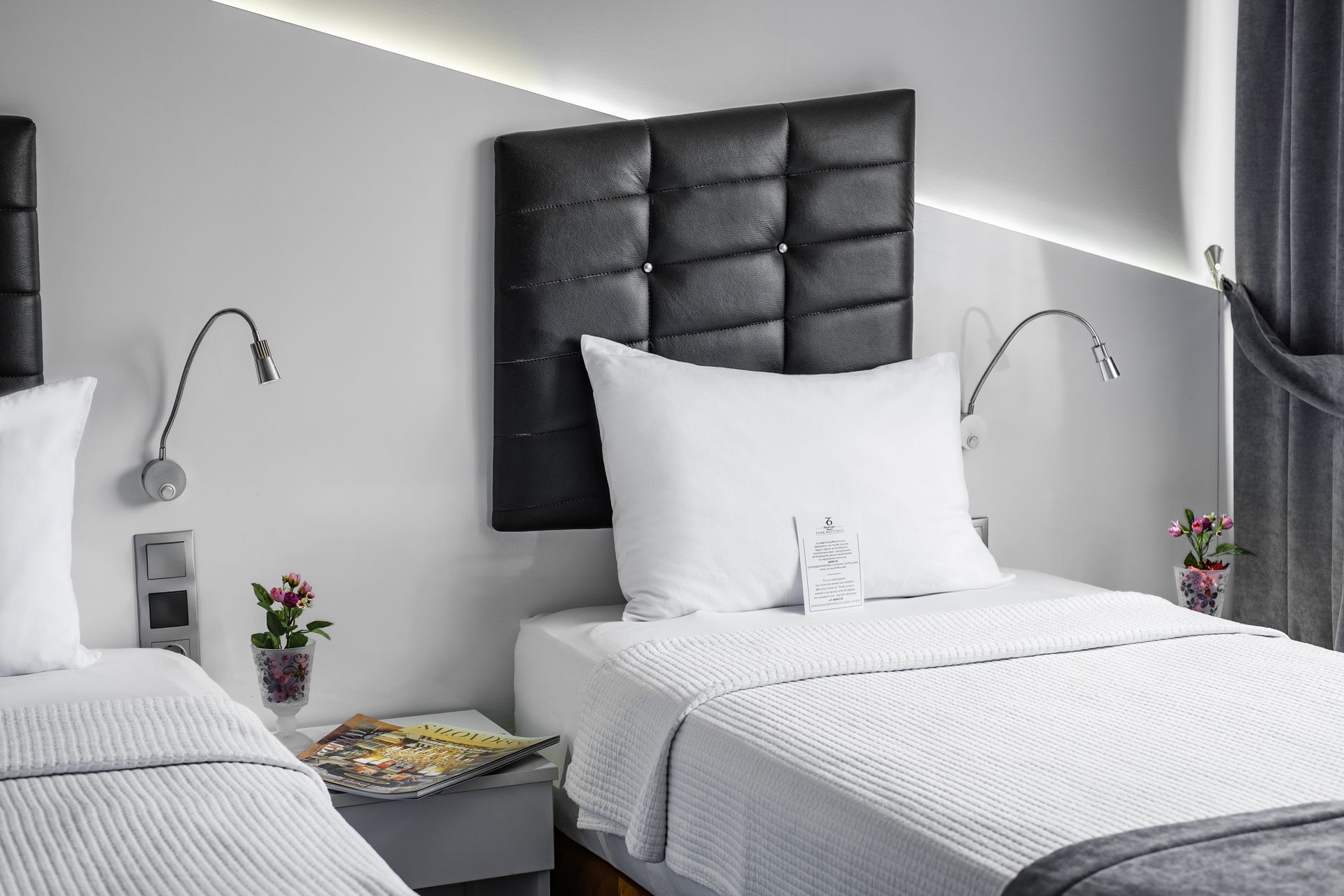 İzmir Park Hotel's two beds in a modern room with dark grey tufted headboards, white linens, and bedside reading lamps.