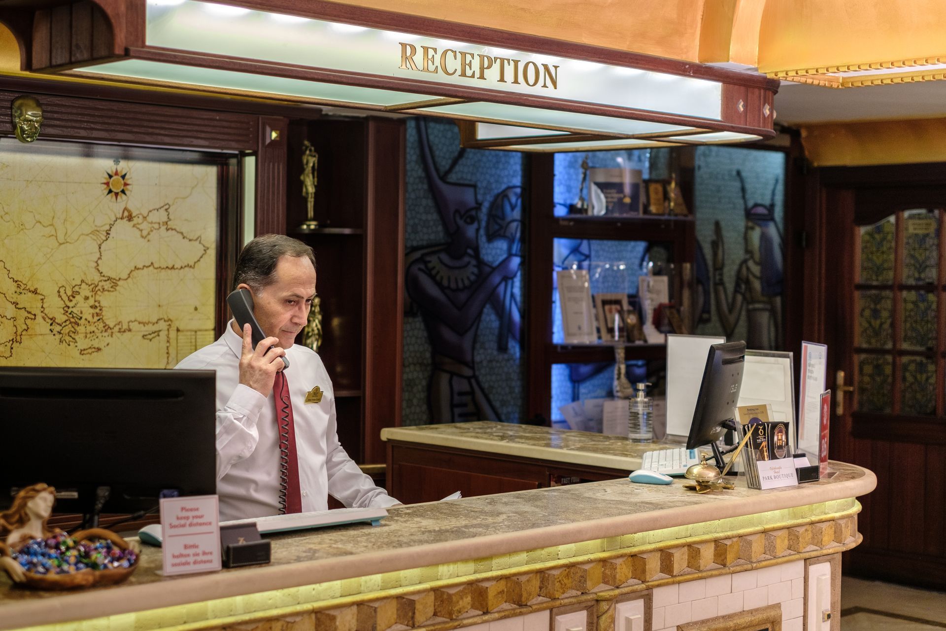 A desk clerk in a dress shirt and tie talks on the phone behind a hotel reception desk decorated with motifs.