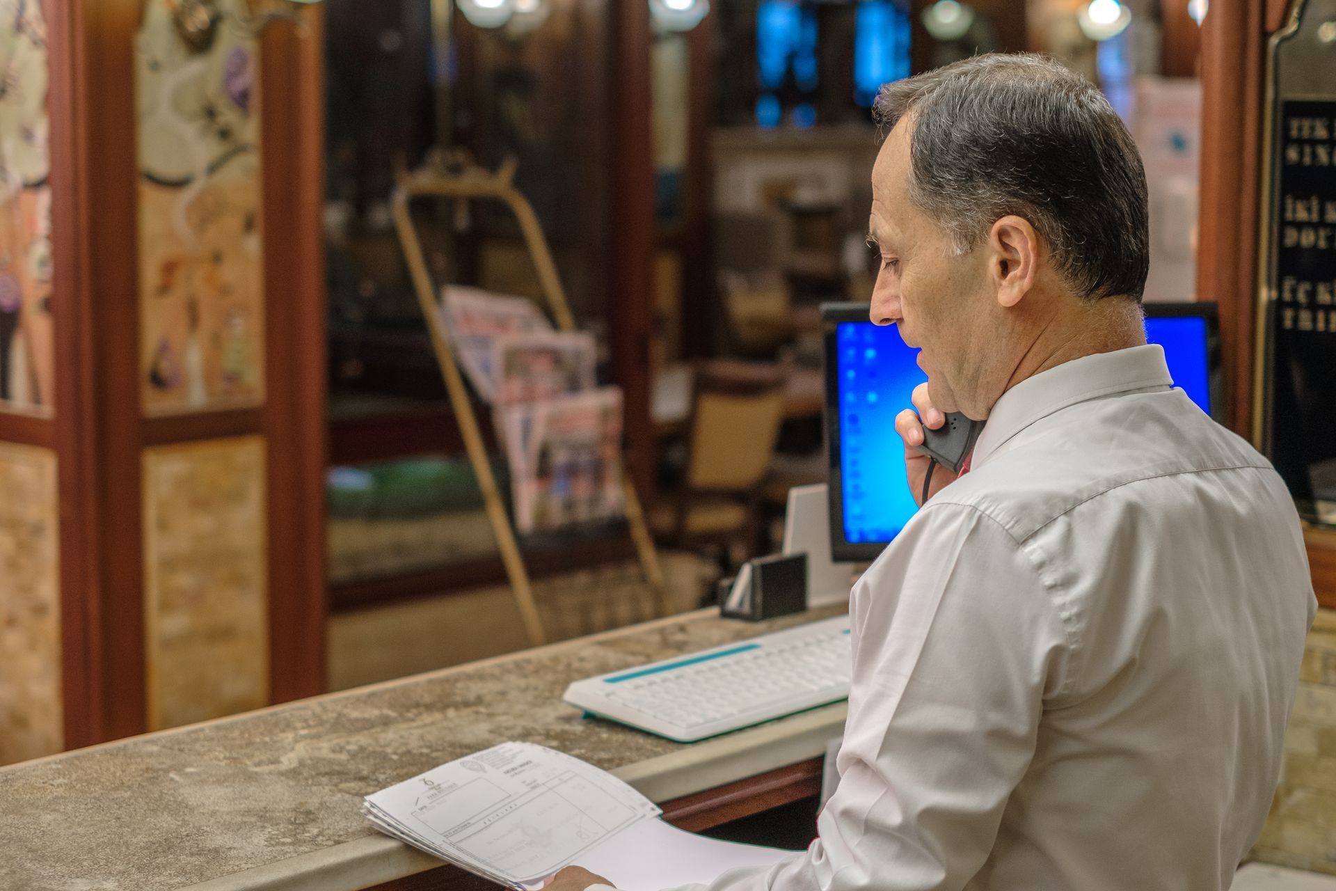 İzmir Park Hotel's person in a white button-down shirt talks on a telephone at a reception desk, holding a notepad. 