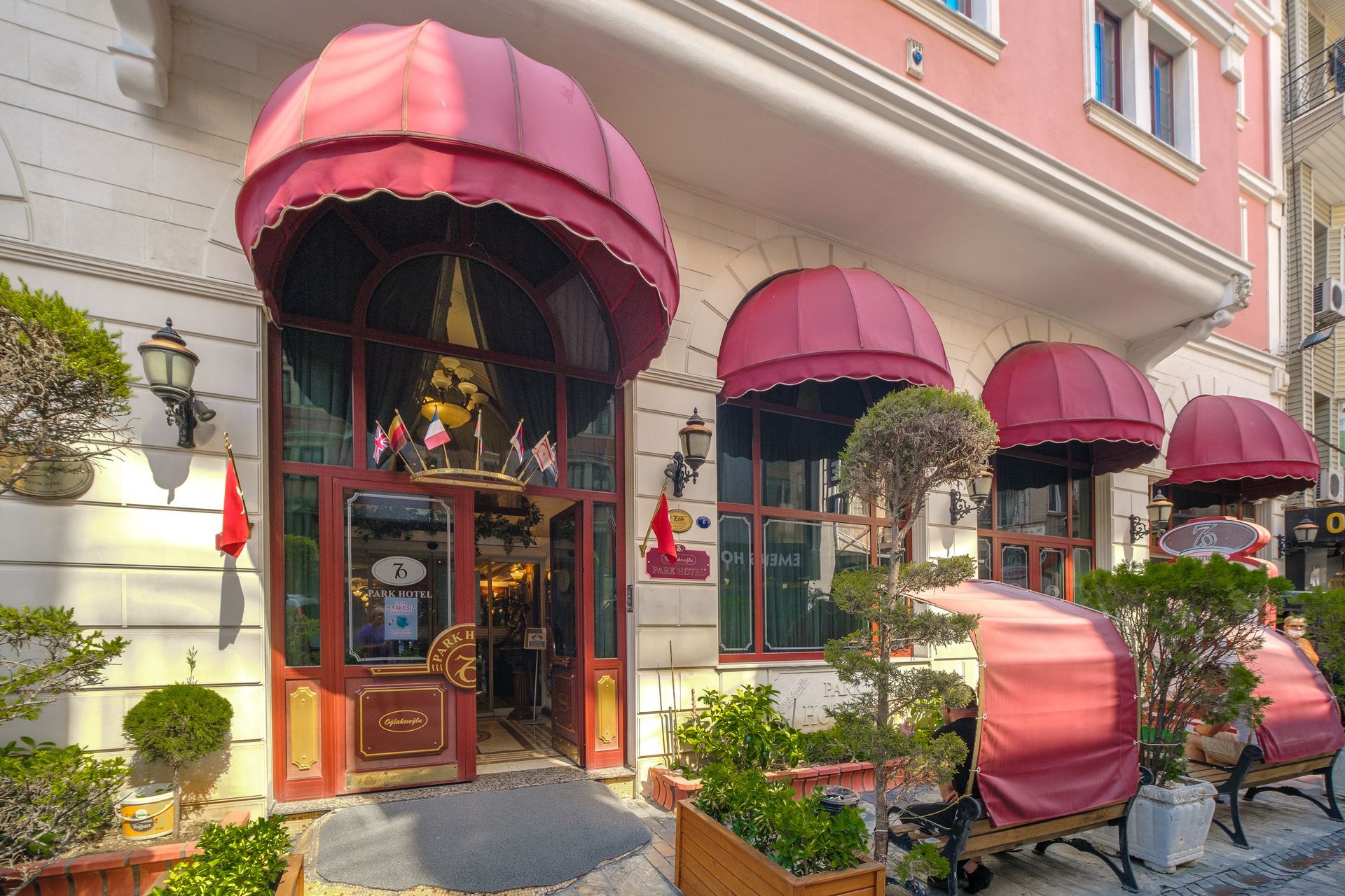 İzmir Park Hotel. Pink building entrance with red domed awnings, potted plants, and outdoor seating on a sidewalk. 