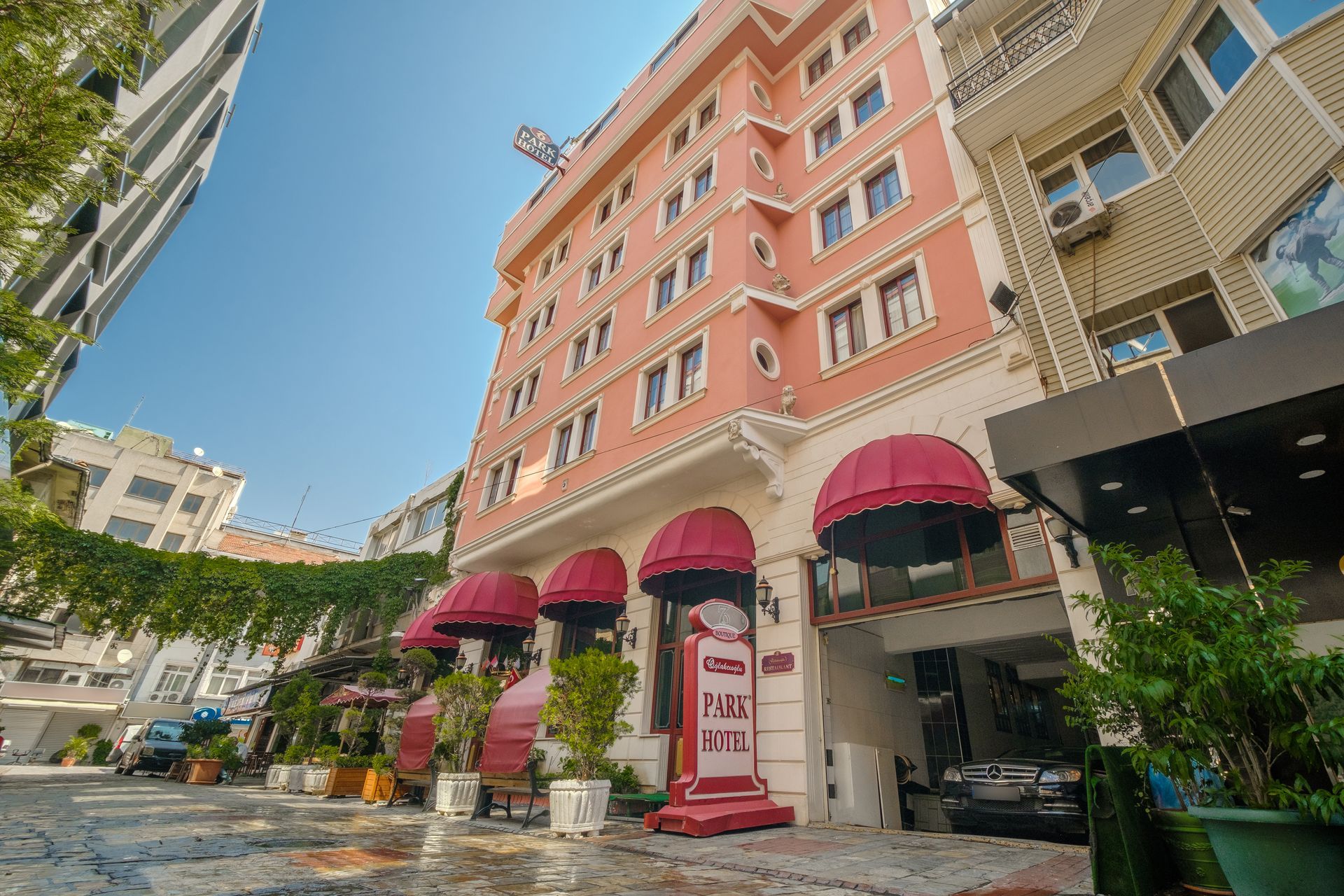 Oğlakçıoğlu İzmir Park Hotel building with red awnings over the entrance and street-level seating under a canopy.