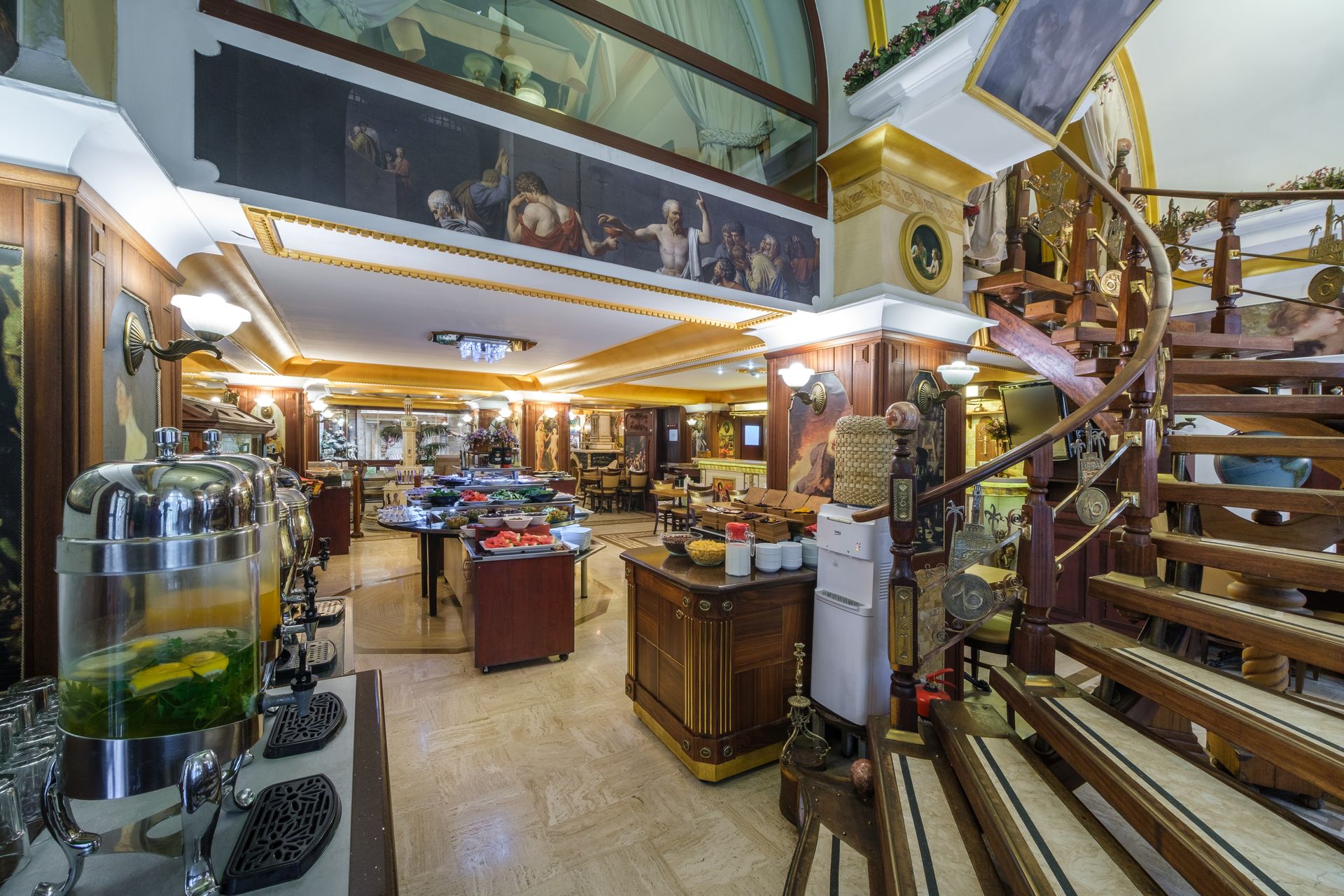 İzmir Park Hotel's breakfast area with a buffet station, a wooden staircase, and a large decorative wall mural.