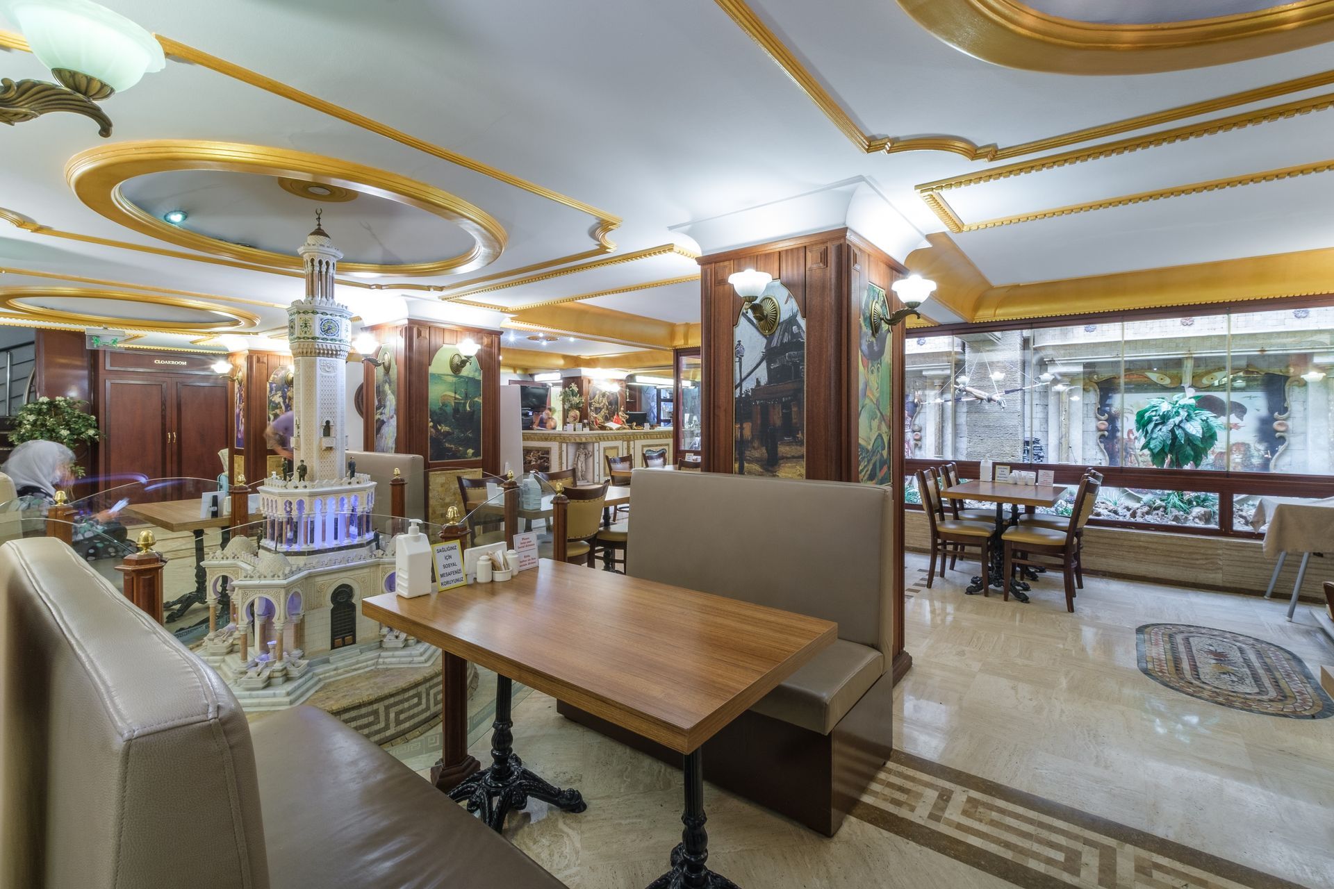 Elegant restaurant interior featuring wooden tables, upholstered booths, ornate gold-trimmed ceilings, and a fountain.