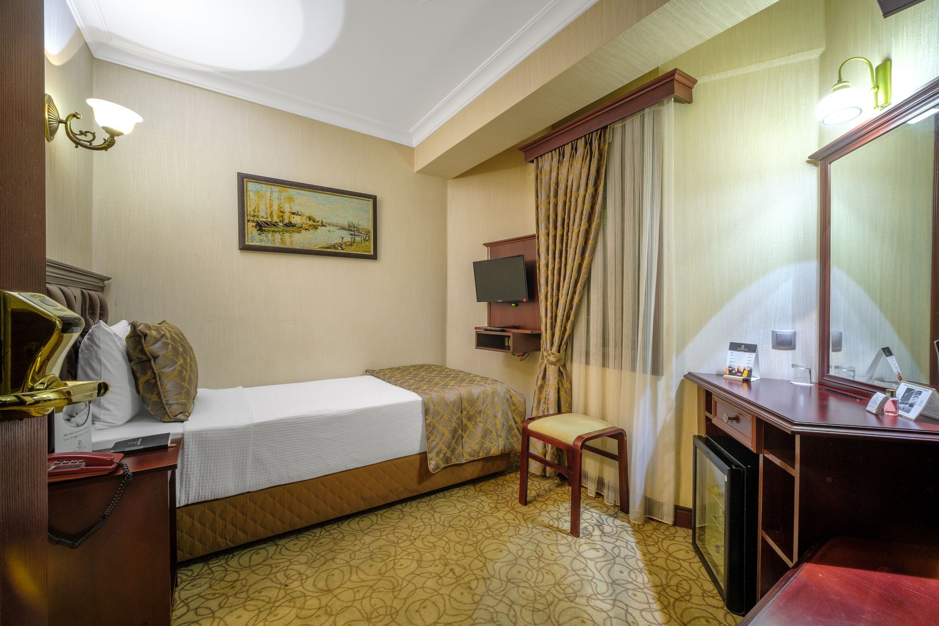 İzmir Park Hotel's compact hotel room with a single bed, tan walls, a small desk with a mini-fridge, and a wall-mounted TV.