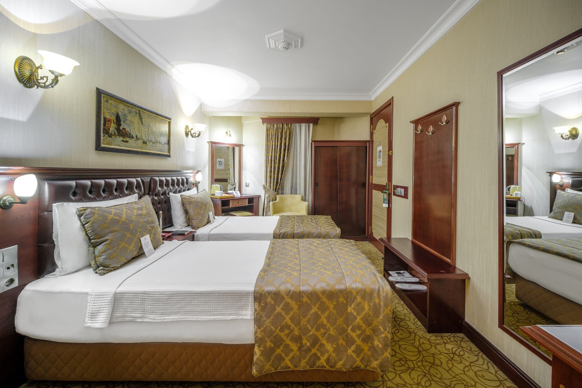 İzmir Park Hotel's bedroom with two beds, matching golden-brown bedding, a large mirror, and warm lighting.