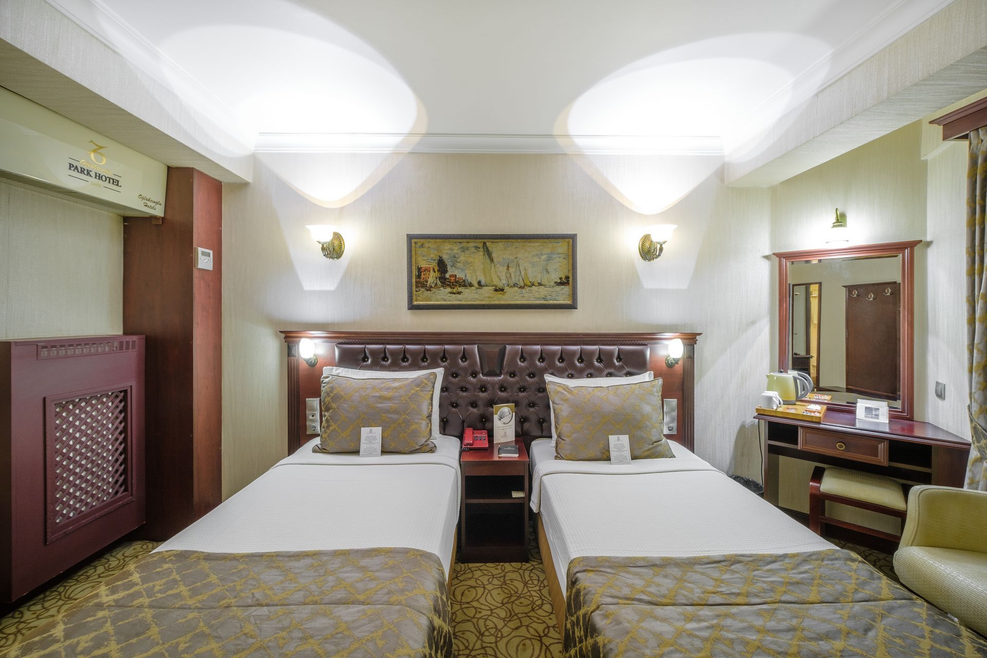 İzmir Park Hotel's room featuring two twin beds with tan patterned covers, a dark wood headboard, and a vanity area.