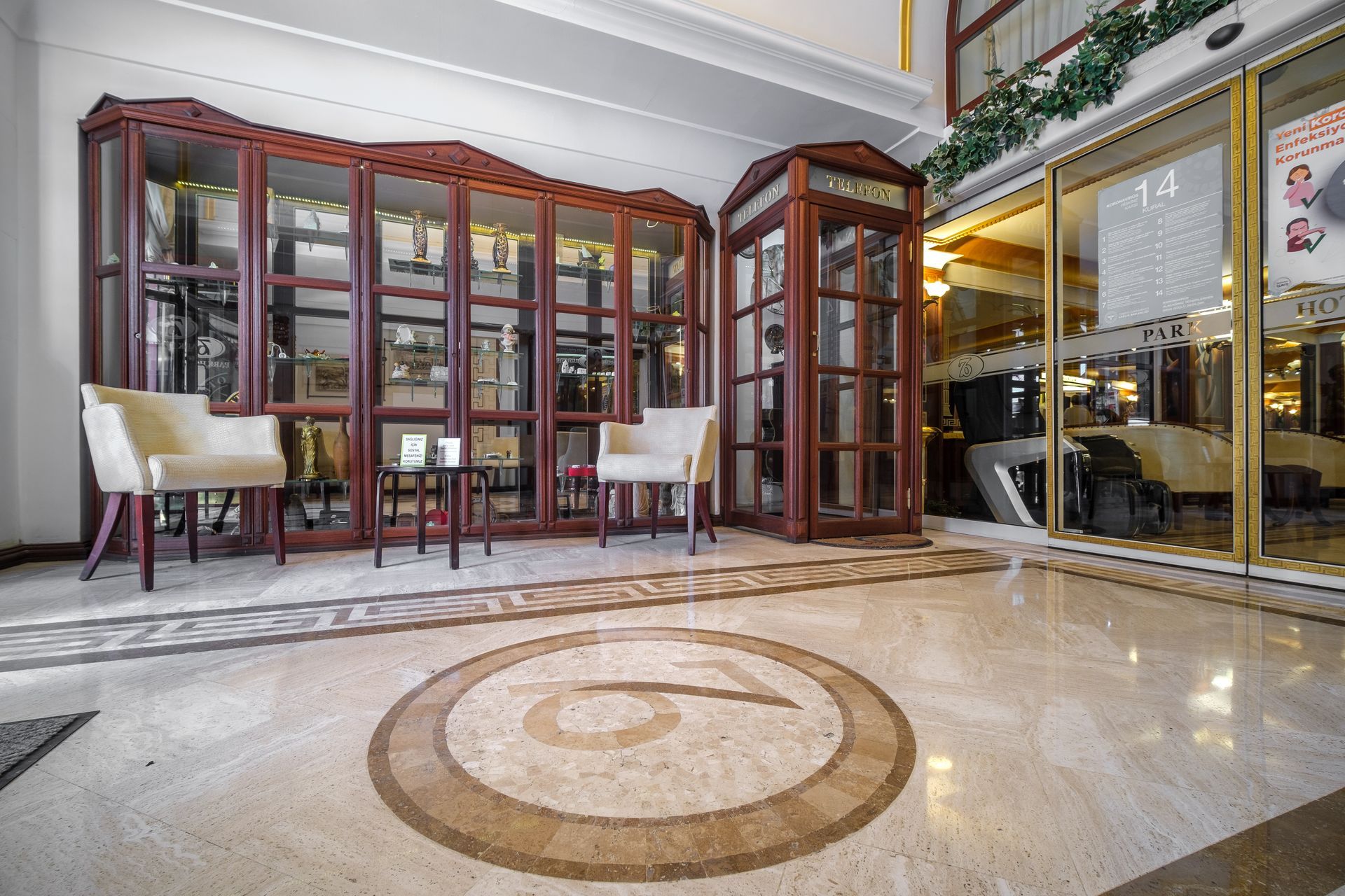 Oğlakçıoğlu İzmir Park Hotel lobby features a large glass display case, a phone booth, two cream chairs, and a small table.