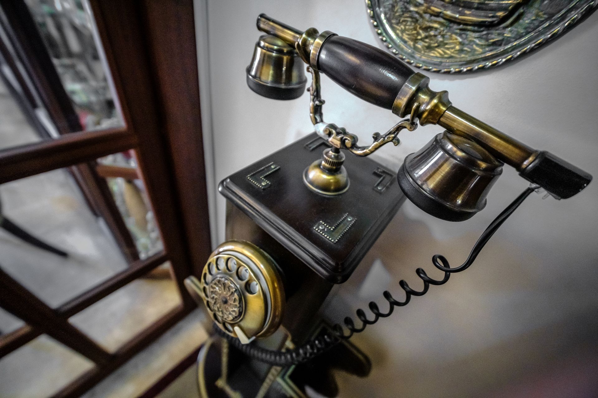 A vintage wooden and brass telephone sits on a stand, featuring a rotary dial and a handset resting on a cradle.