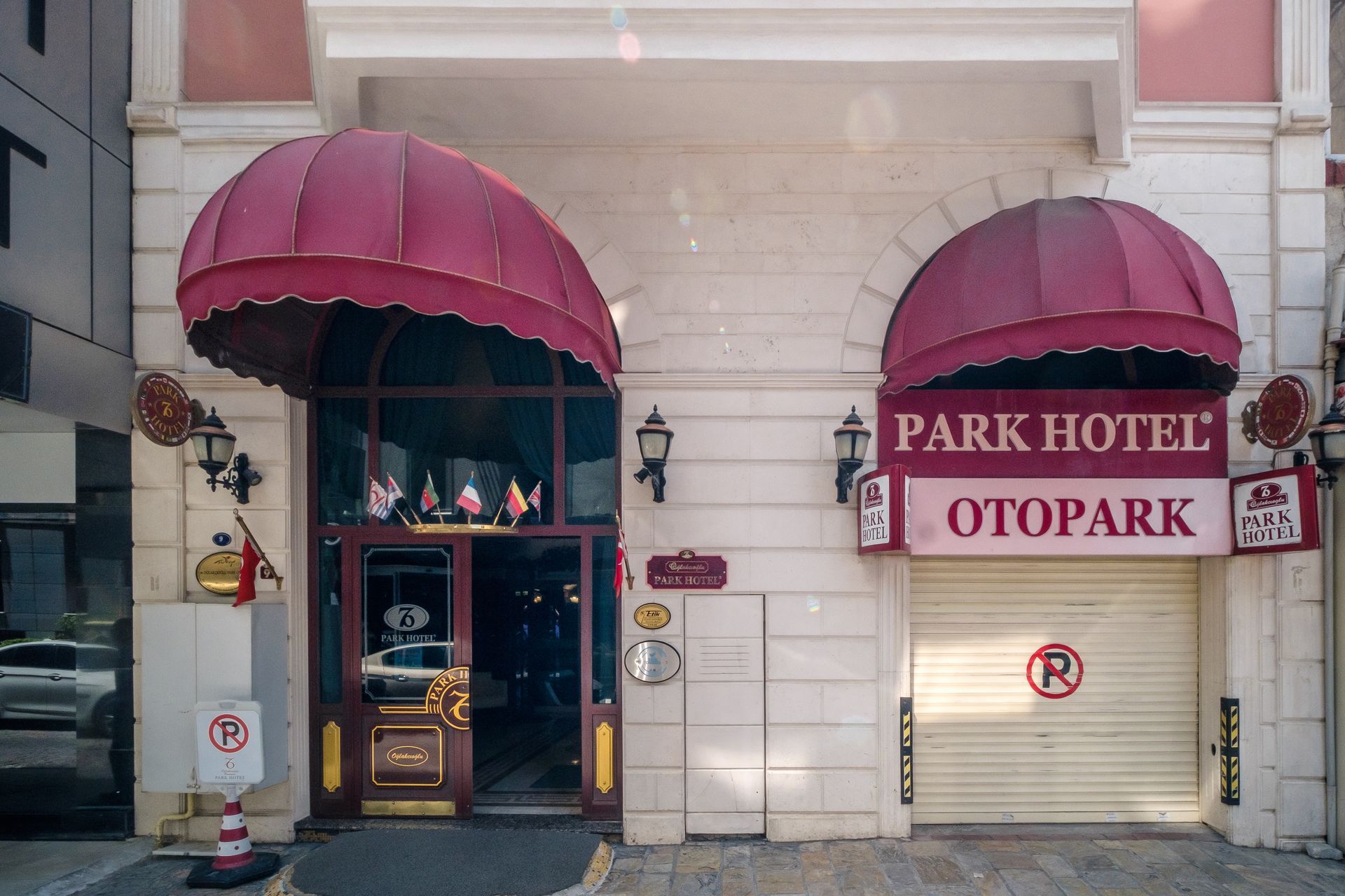 The exterior of İzmir Park Hotel, featuring a cream facade, a dark glass entrance, and a closed parking garage.