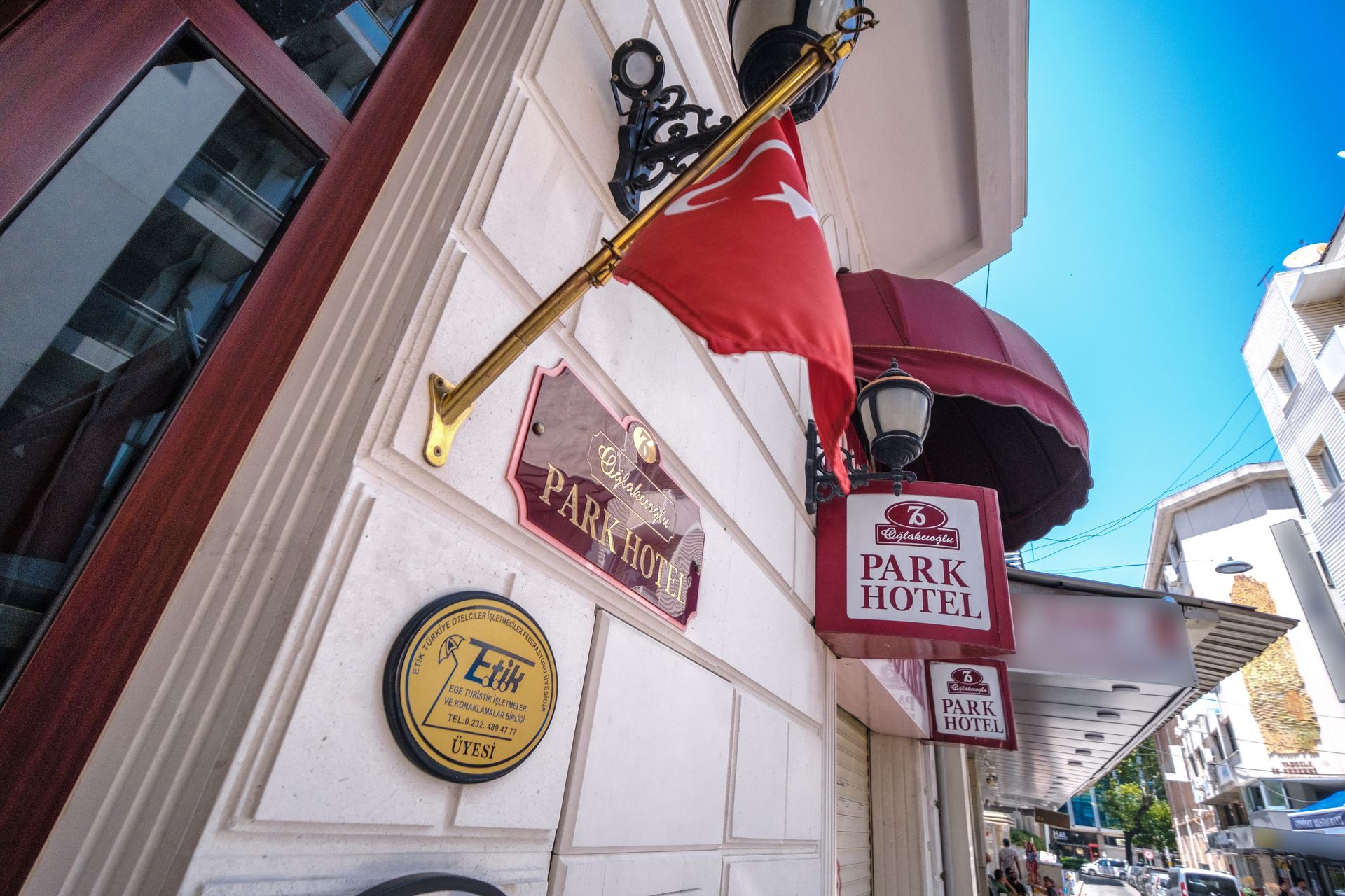 A low-angle view of the exterior of Park Hotel with a red Turkish flag, signage, and a circular emblem on a white wall.